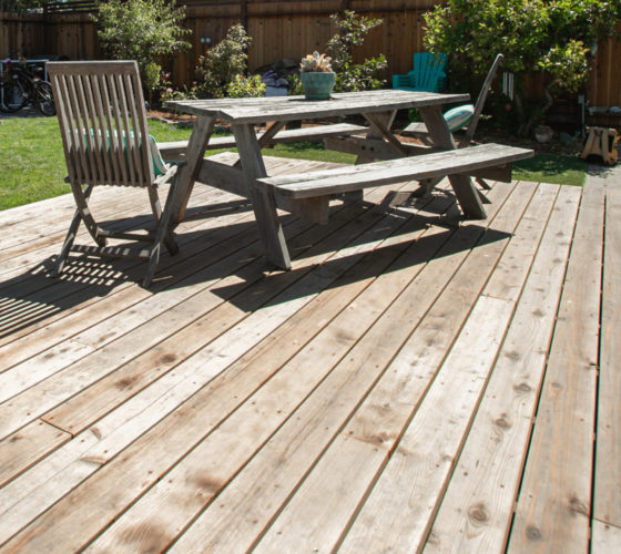 A large wooden deck with a picnic table and a deck chair on top.