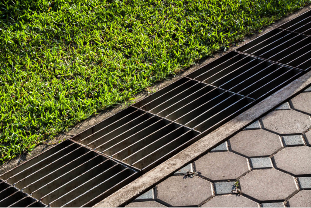 A drainage system runs alongside a stone pathway and separates it from a bright green lawn.
