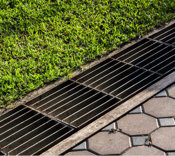 A drainage system runs alongside a stone pathway and separates it from a bright green lawn.