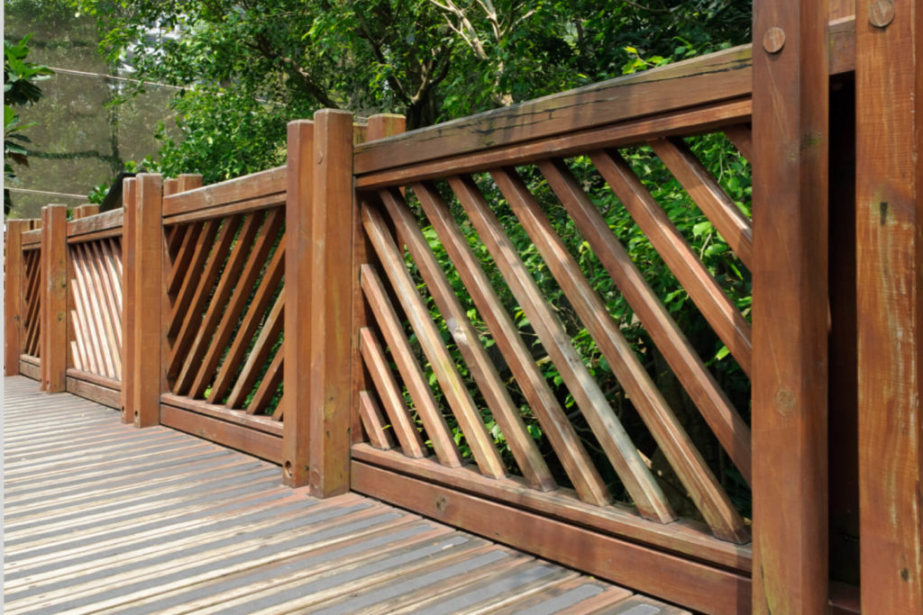 A sturdy, wooden fence runs alongside a pathway made of wooden beams.