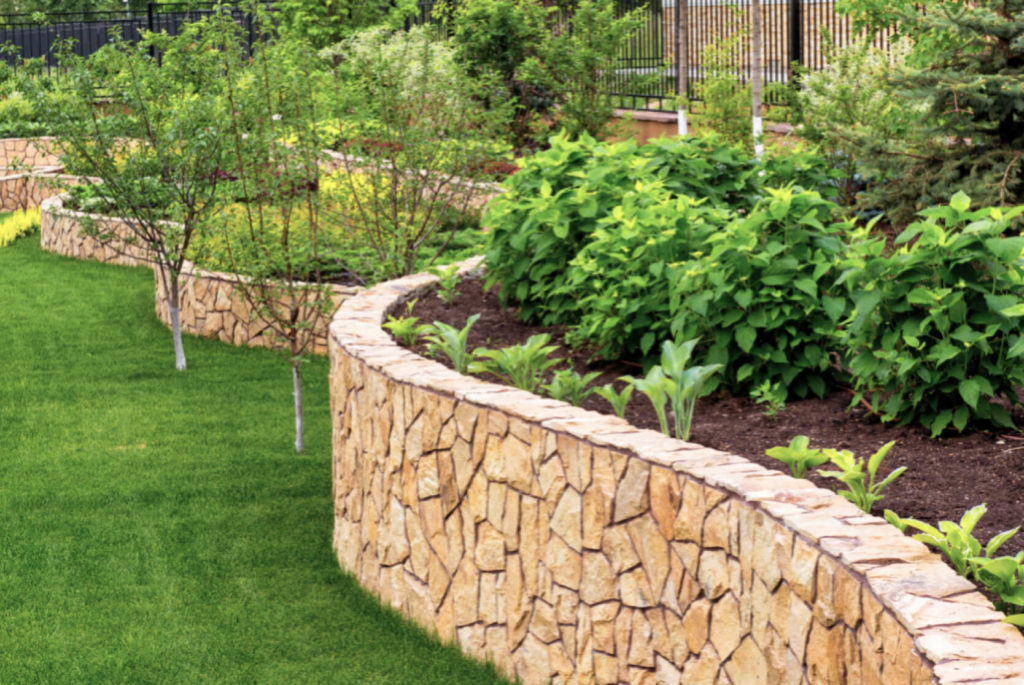 A large stone retaining wall borders an elevated garden on one side and a perfectly manicured lawn on the other.