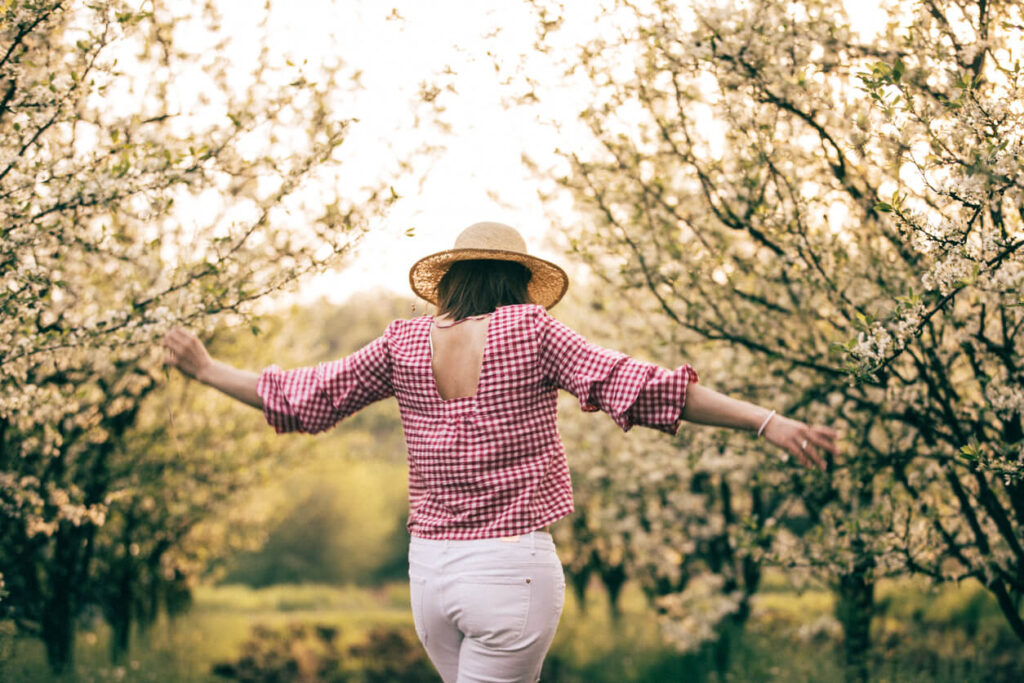 A photo of a woman wearing a pink shirt, walking through an orchard.