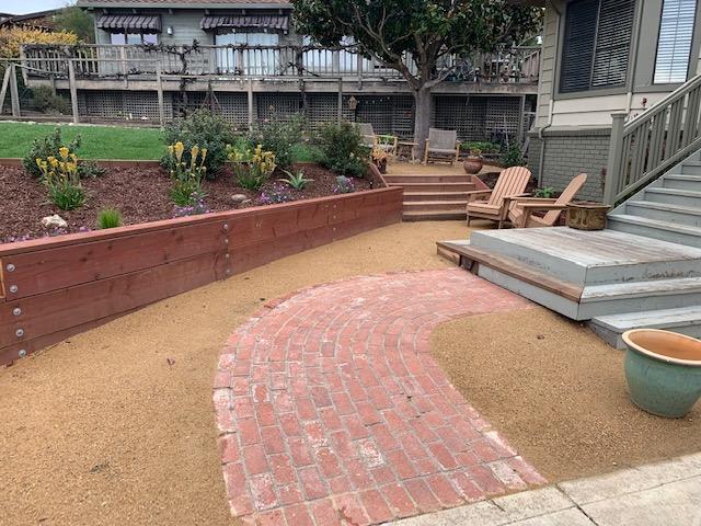 A modern backyard with a horizontal timber retaining wall, curved brick walkway, and small patio seating area.