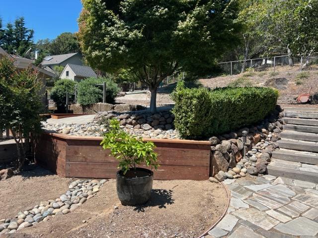 A landscaped yard featuring a wooden retaining wall accented with river rocks, shrubs, and stone steps.