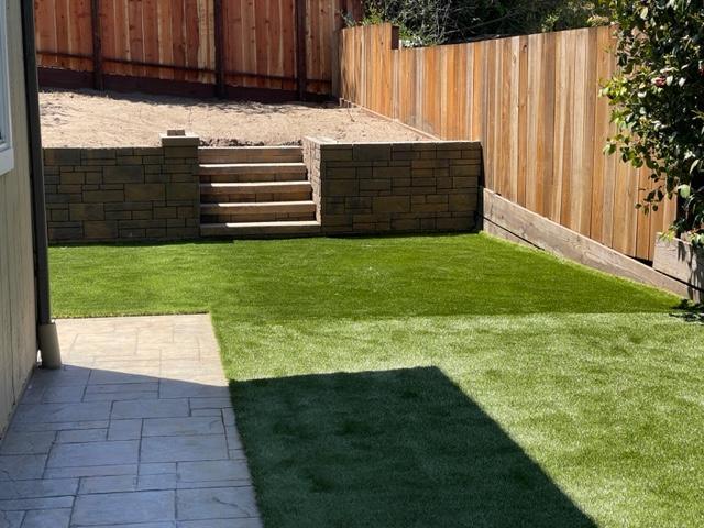 A neatly graded yard with a concrete block retaining wall supporting a higher dirt level above a green lawn.