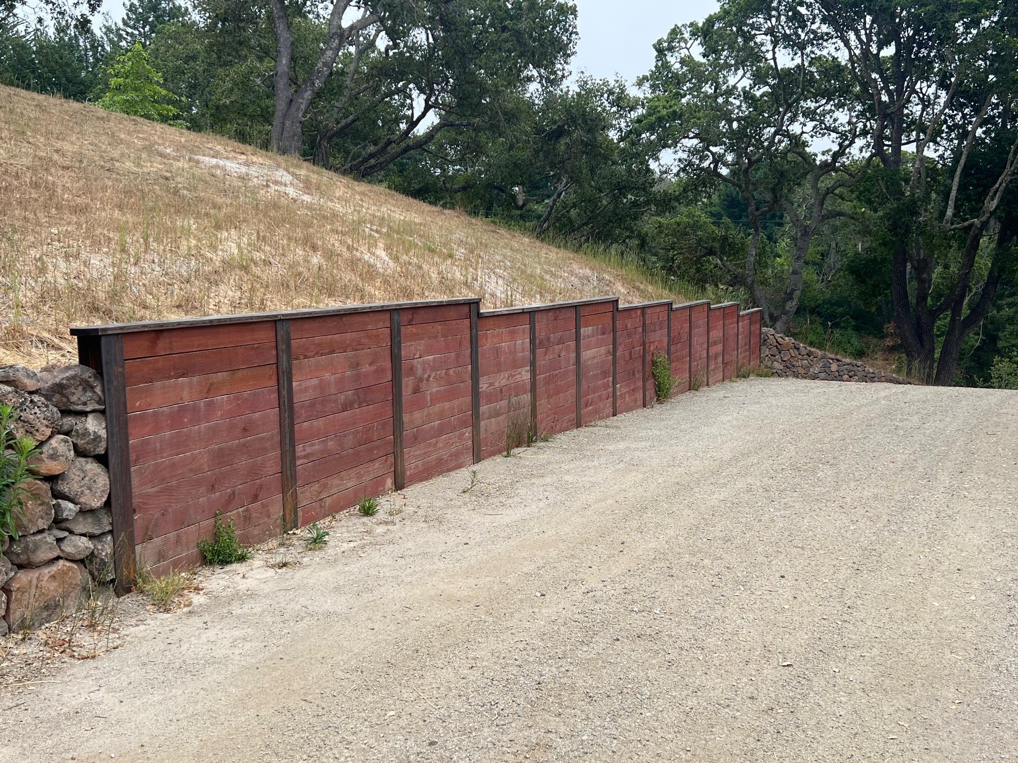 Long timber retaining wall for sloped yard along gravel driveway